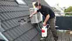 Schädlingsbekämpfer der PCS GmbH verteilt Marder Abwehr Präparate unter den Dachpfannen auf einem Hausdach.